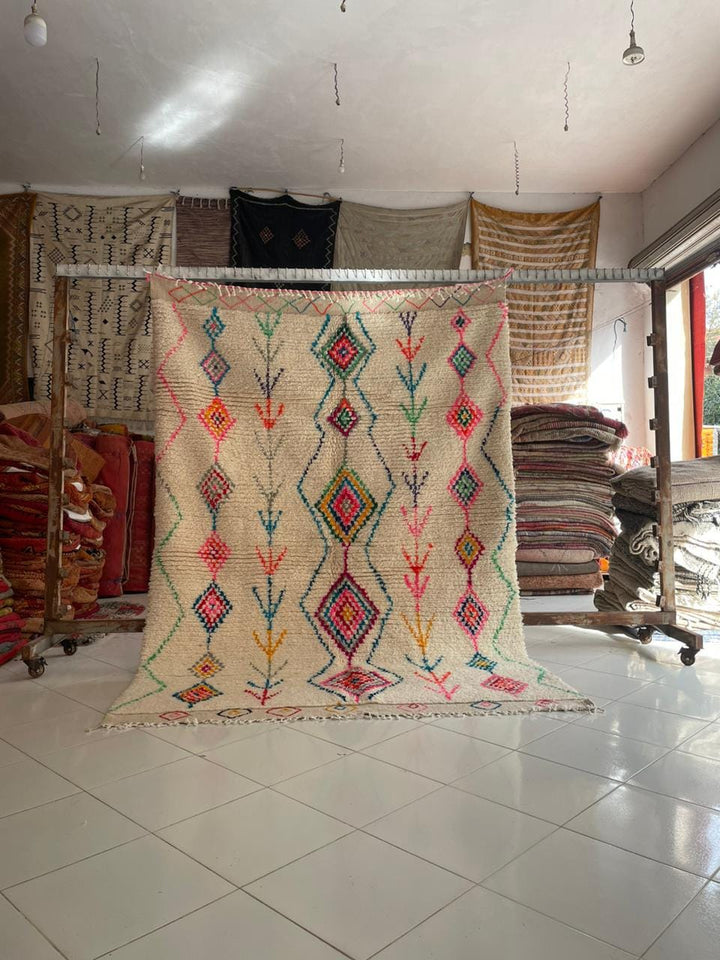 Lifestyle shot of a colorful vintage Moroccan rug with geometric patterns in cream, red, blue, and green.