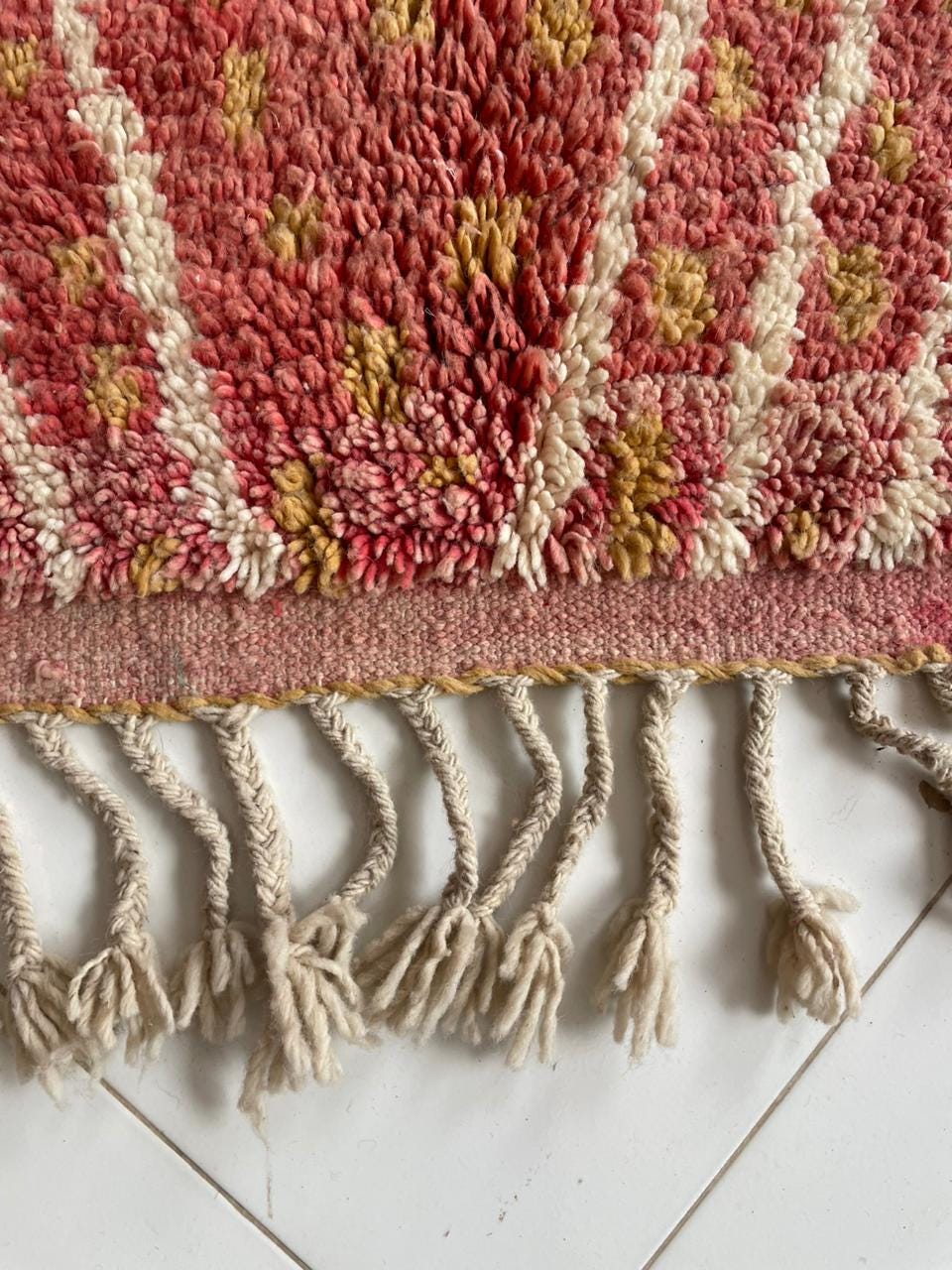 Detail shot of a vintage Moroccan rug showcasing fringe detail and a textured pattern in red, cream, and gold.