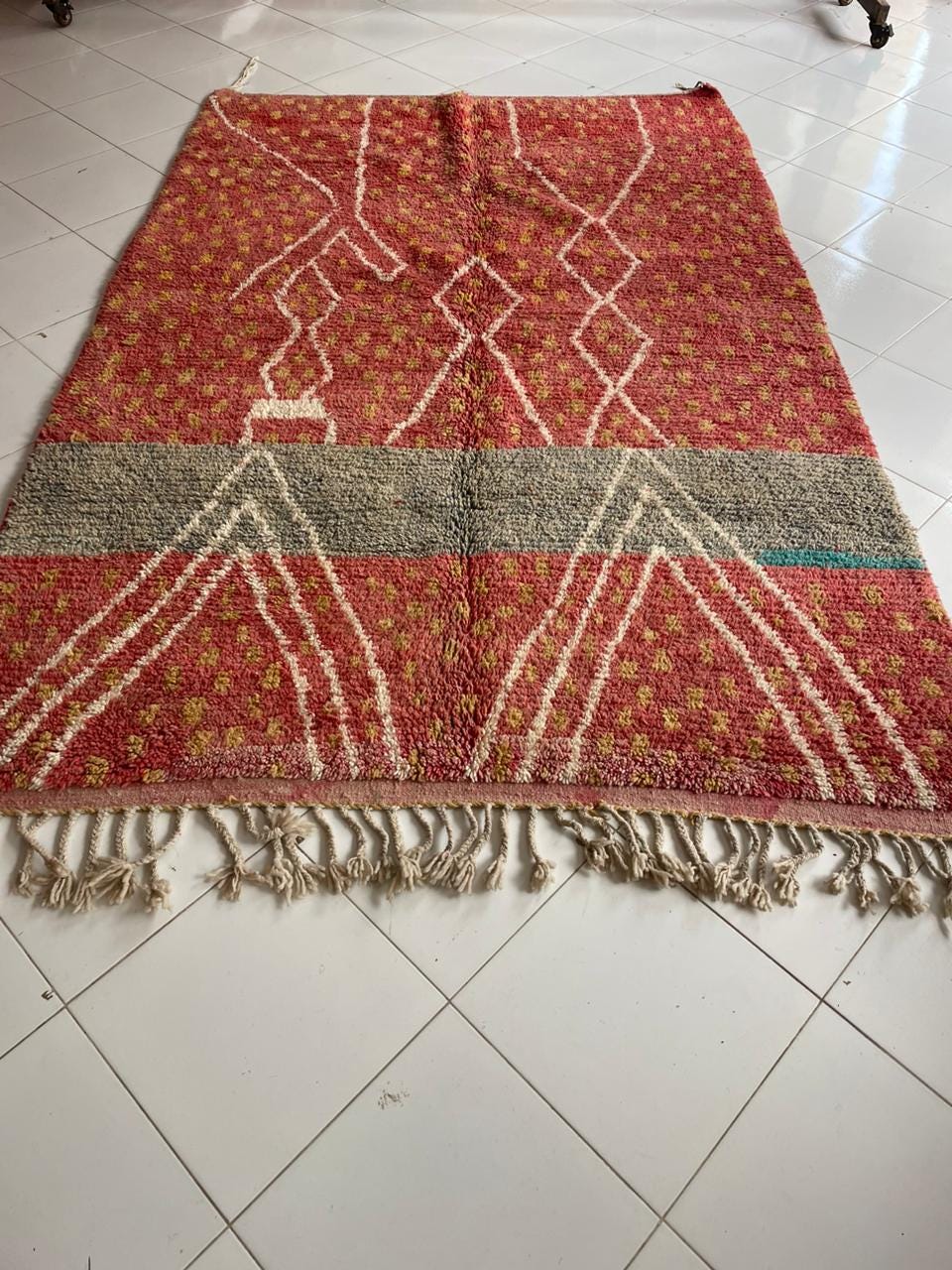 Lifestyle image of a vintage Moroccan rug displaying red, blue, and white colors with fringe edges.