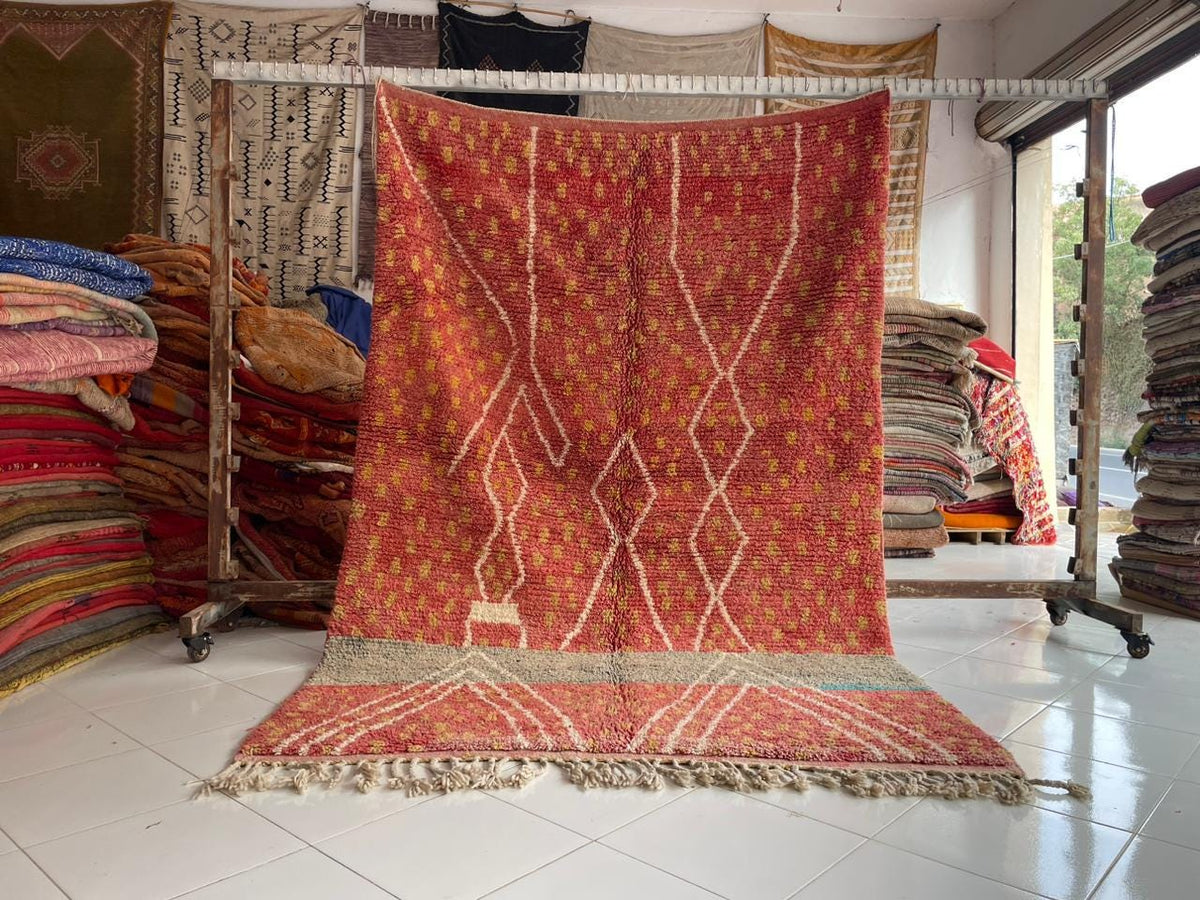 Lifestyle shot of a large vintage Moroccan rug featuring orange, red, and cream colors with a decorative pattern.