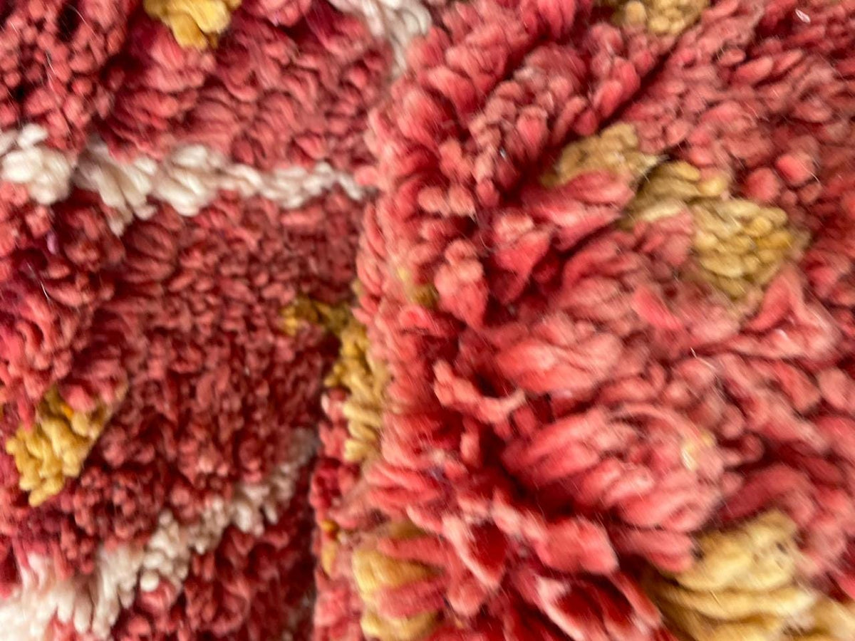 Close-up of plush fibers and rich colors on a vintage Moroccan rug in red and gold.