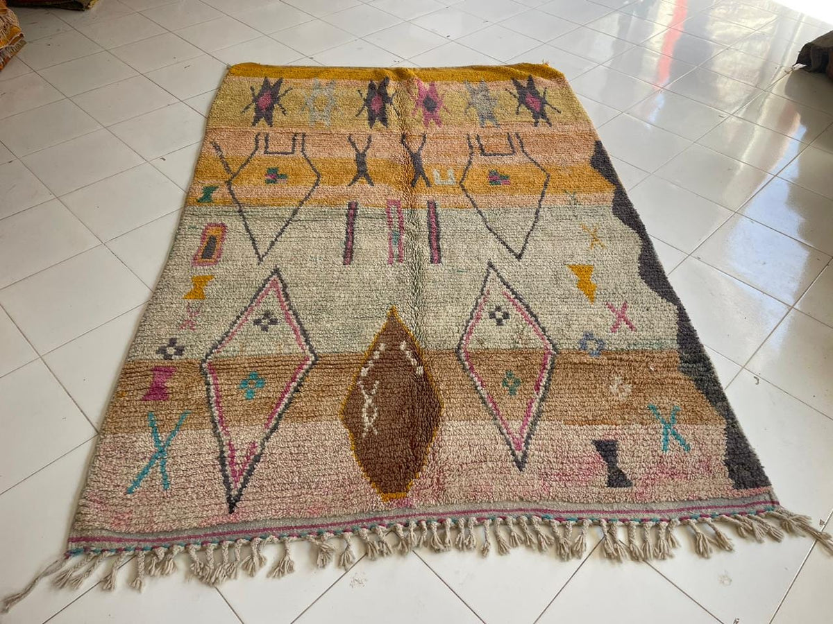 Top view of a vintage Moroccan rug with geometric designs in yellow, pink, and beige.