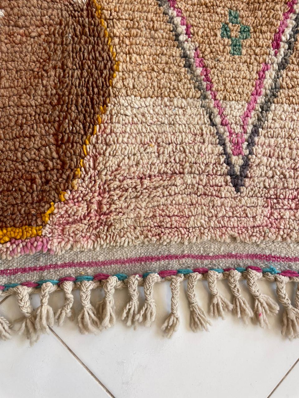 Detail shot of a woven textile featuring fringe and geometric patterns in brown, pink, and blue.
