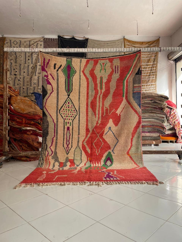 Lifestyle shot of a vintage Moroccan rug featuring geometric patterns in red, beige, and green.
