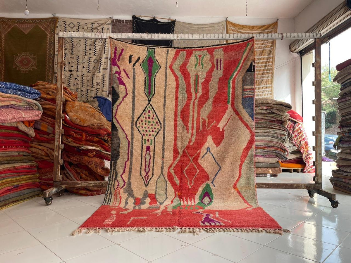 Lifestyle image of a vintage Moroccan rug with an abstract design in red, beige, blue, and green.