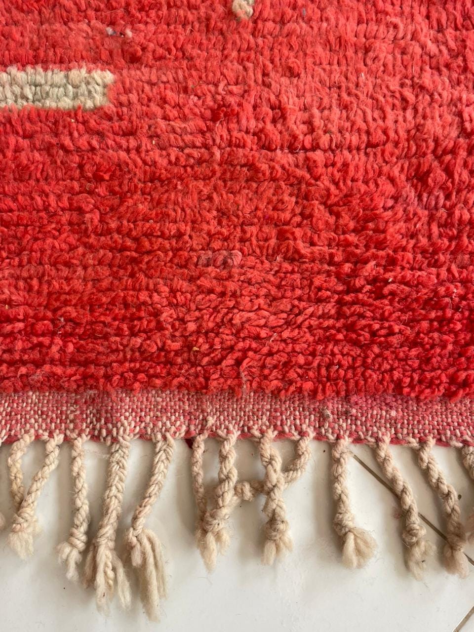 Detail shot of a red woven rug featuring fringe edges and a textured pattern.