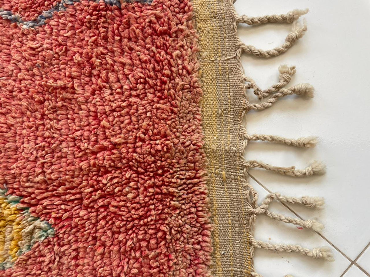Detail shot of a red vintage Moroccan rug showcasing its abstract patterns and fringe edges.