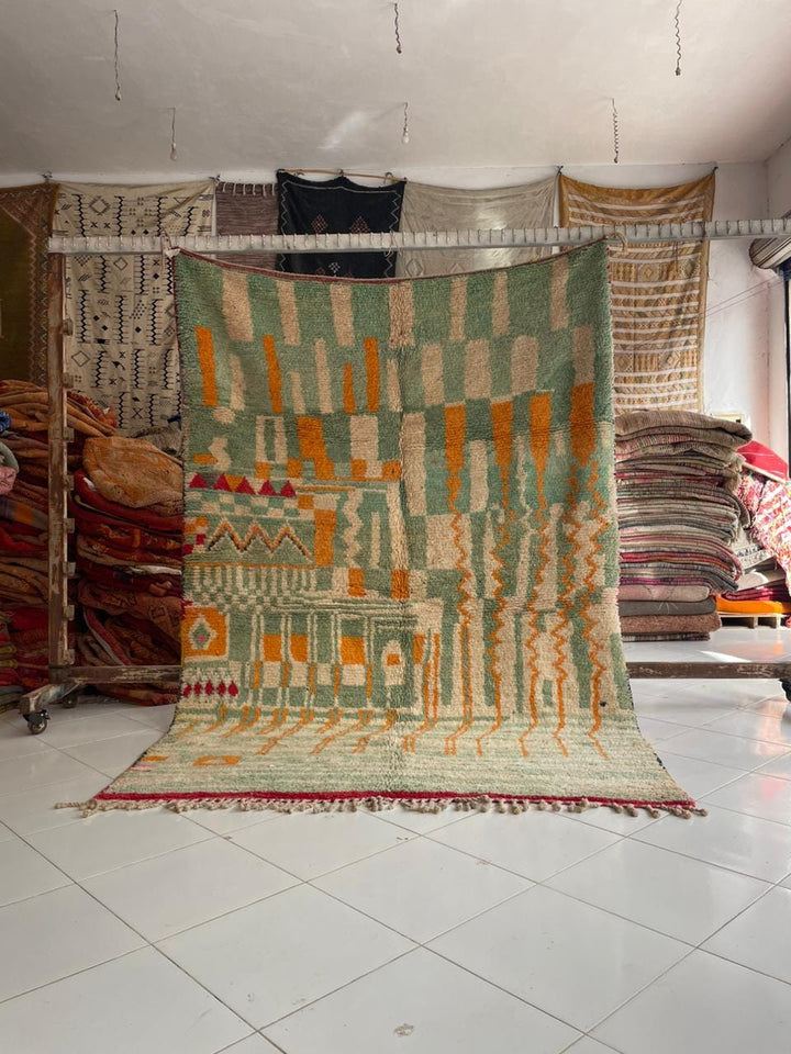 Lifestyle shot of a vintage Moroccan rug featuring geometric patterns in green and orange.