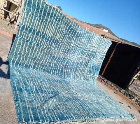 Lifestyle shot of a large turquoise Moroccan rug with a textured surface.