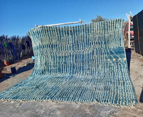 Detail close-up of a turquoise Moroccan rug showcasing a striped pattern and fringe edges.
