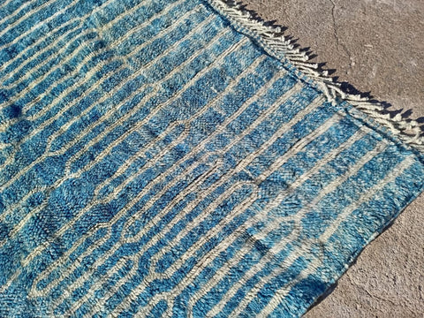 Detail close-up of a turquoise Moroccan rug featuring a fringed edge and striped design.