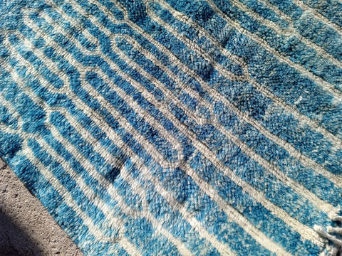 Close-up of a turquoise Moroccan rug displaying a striped pattern and textured surface.