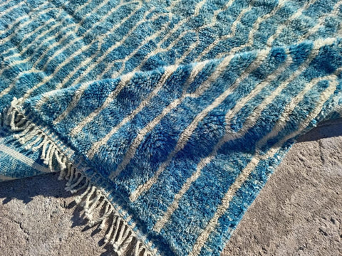Detail close-up of a turquoise Moroccan rug with a striped pattern and fringe edges.