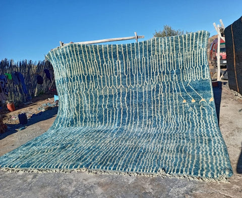 Lifestyle shot of a turquoise Moroccan rug with a textured pattern in a natural setting.