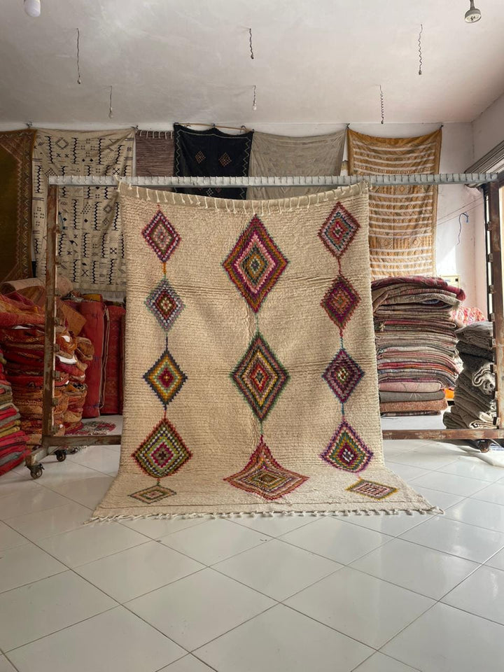 Lifestyle shot of a vintage Moroccan rug with geometric patterns in beige, red, and green.