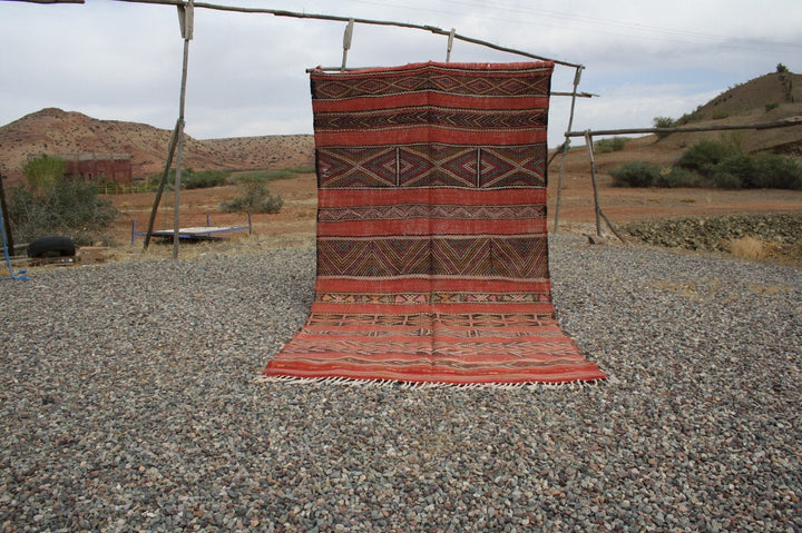 Lifestyle shot of a vintage kilim rug featuring geometric patterns in red, black, and orange.