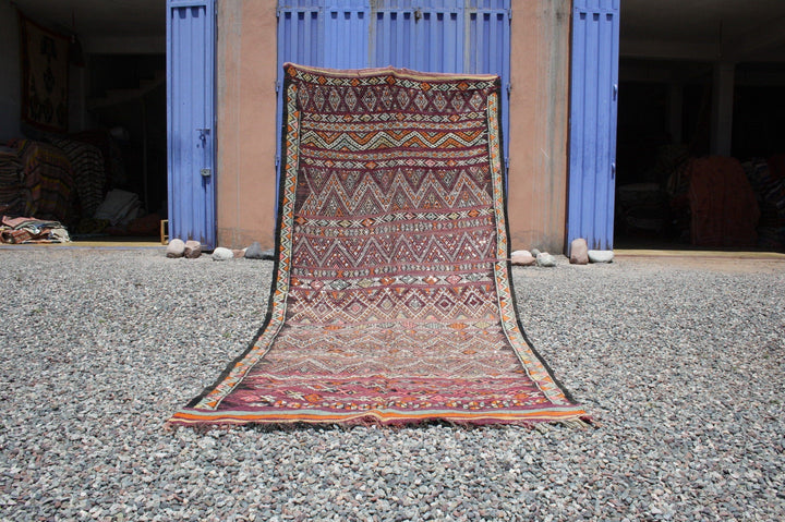 Lifestyle shot of a vintage kilim rug with geometric patterns in red and orange tones.