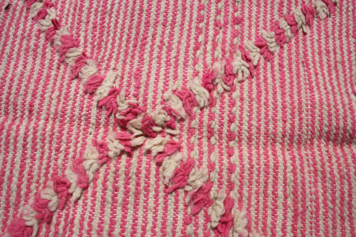 Close-up of a pink kilim rug displaying a striped pattern with embroidered details.