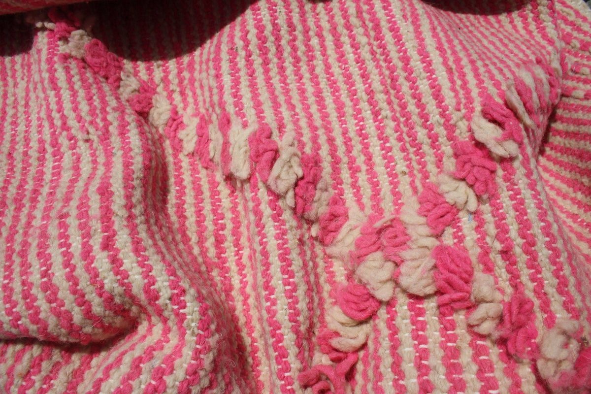 Detail view of a pink kilim rug featuring a striped pattern and embroidered accents.