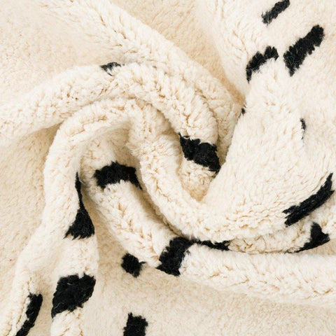 Detail view of the textured fabric and black patterns on the cream Moroccan rug.