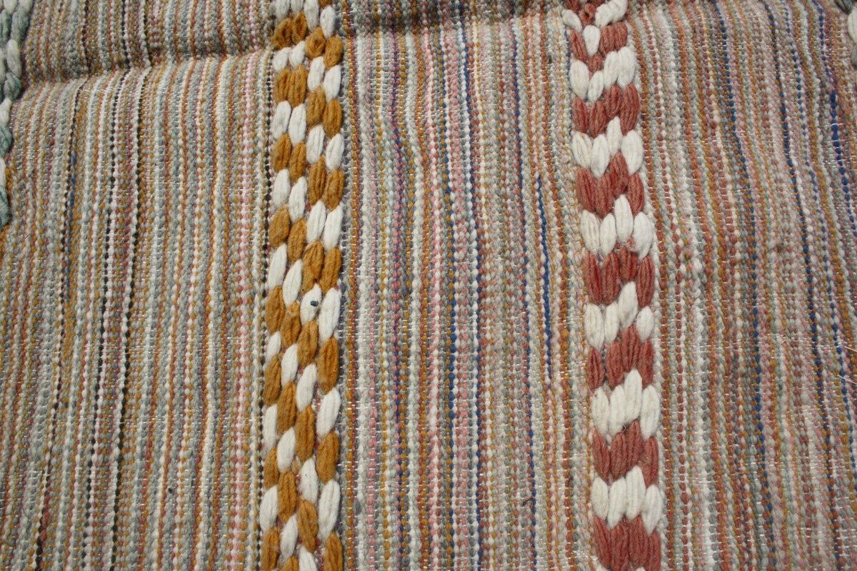 Detail shot of a Moroccan kilim rug featuring woven patterns in beige, orange, and red.