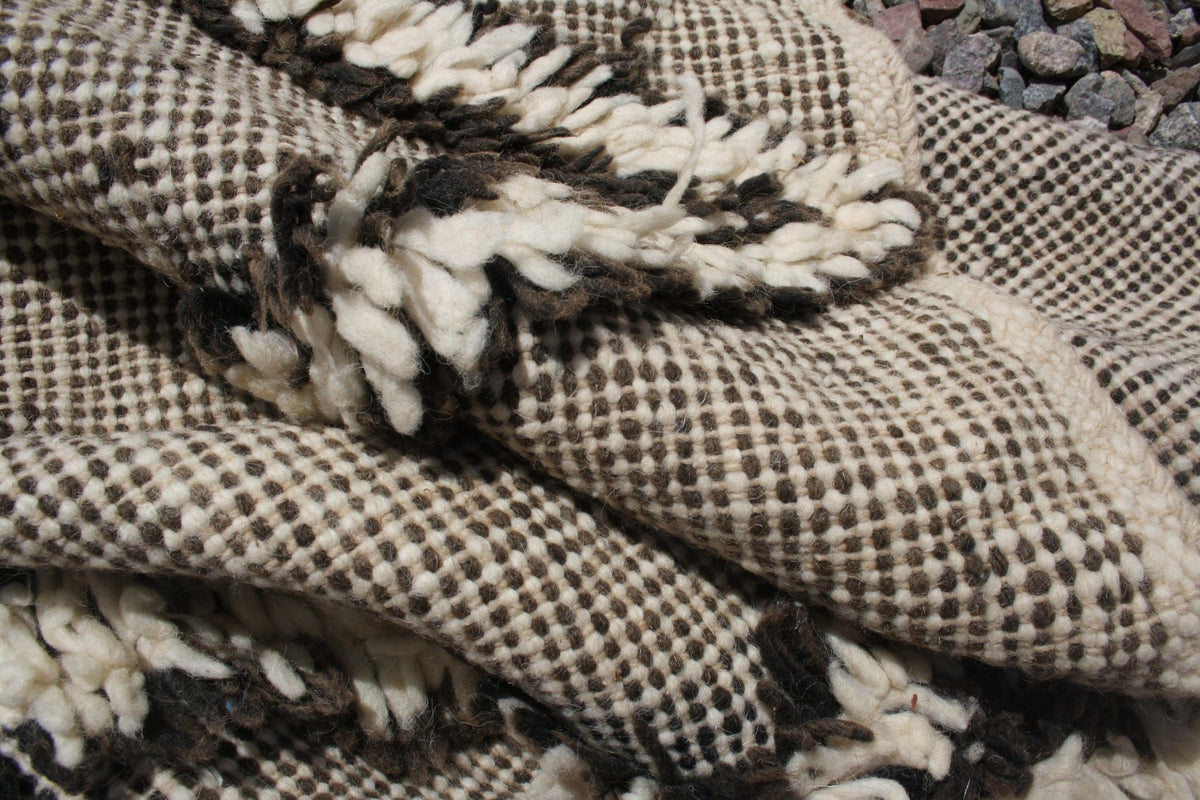 Detail shot of a Moroccan kilim rug displaying a layered texture and woven design in black, white, and beige.