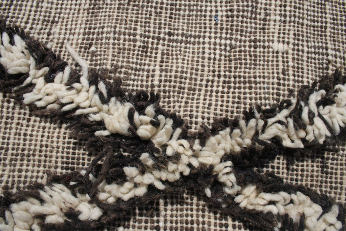 Close-up view of a Moroccan kilim rug with a textured weave in black, white, and beige colors.