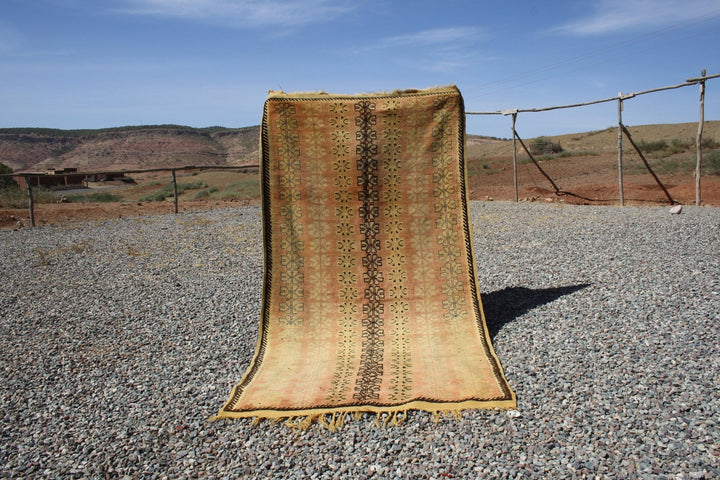 Lifestyle shot of a vintage kilim runner featuring brown and gold woven textures with fringe edges.