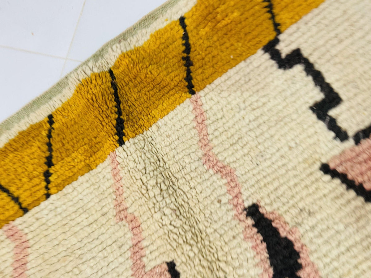 Detail shot of a vintage Moroccan rug showcasing geometric design in yellow, pink, and black.
