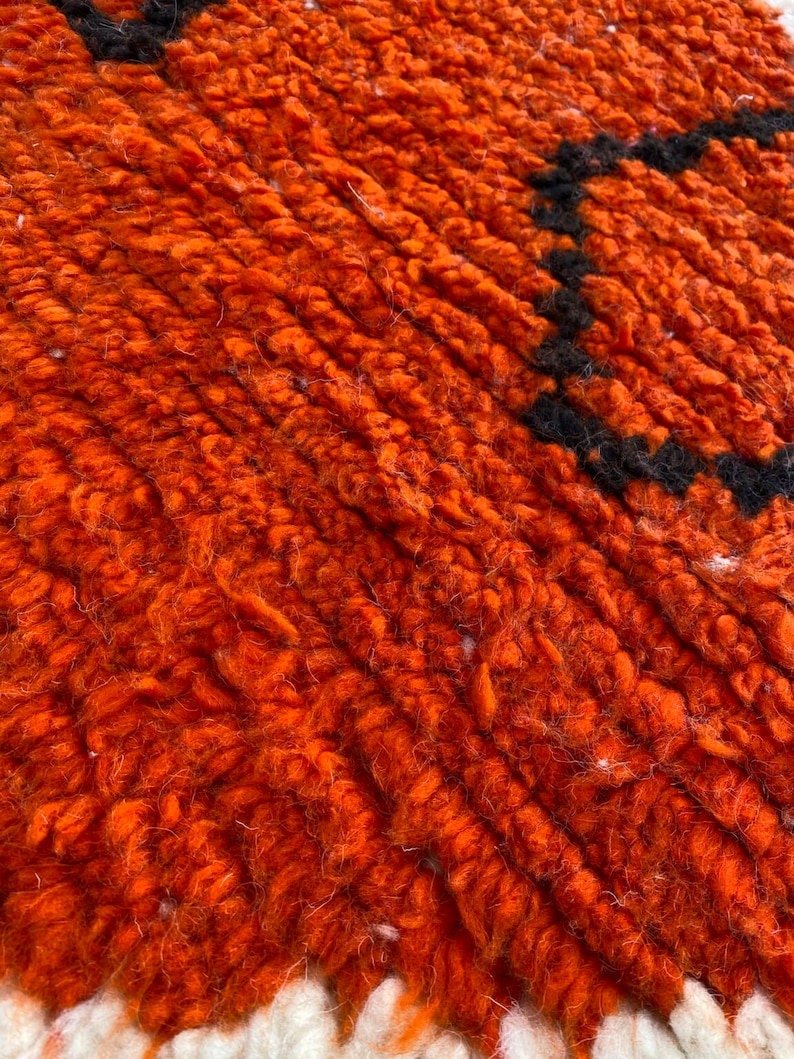 Detail shot of an orange and black abstract line pattern on the Beni Ourain rug.