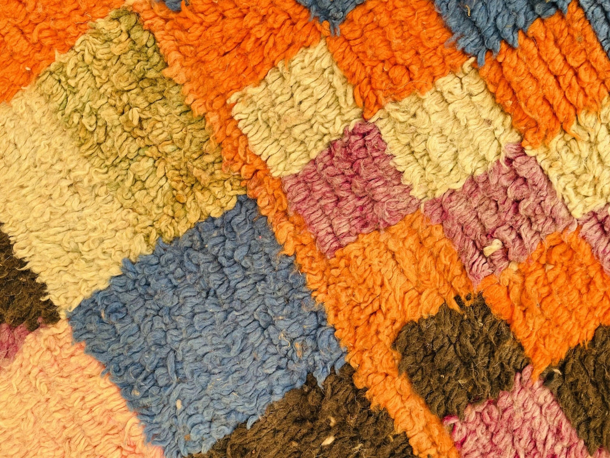 Detail view of a vintage Moroccan rug featuring geometric patterns in orange and purple.