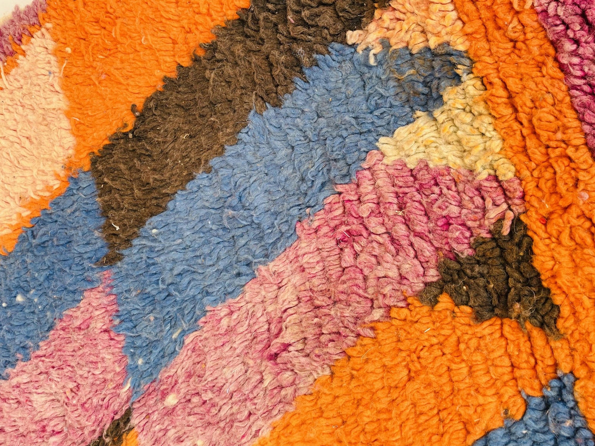 Detail shot of a vintage Moroccan rug displaying abstract patterns in orange, blue, and pink.