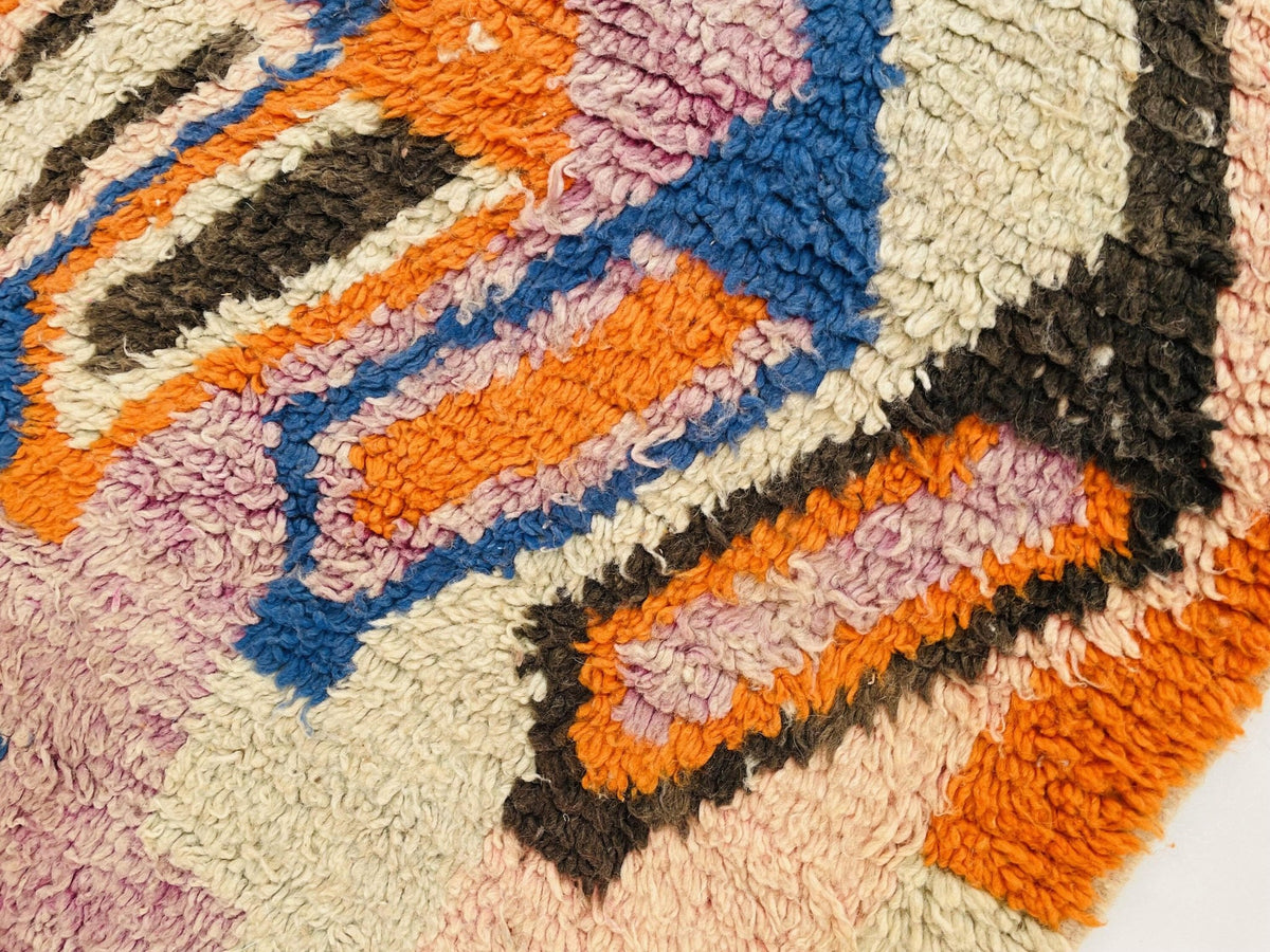 Detail close-up of colorful squares on a vintage Moroccan rug in orange, blue, and pink.