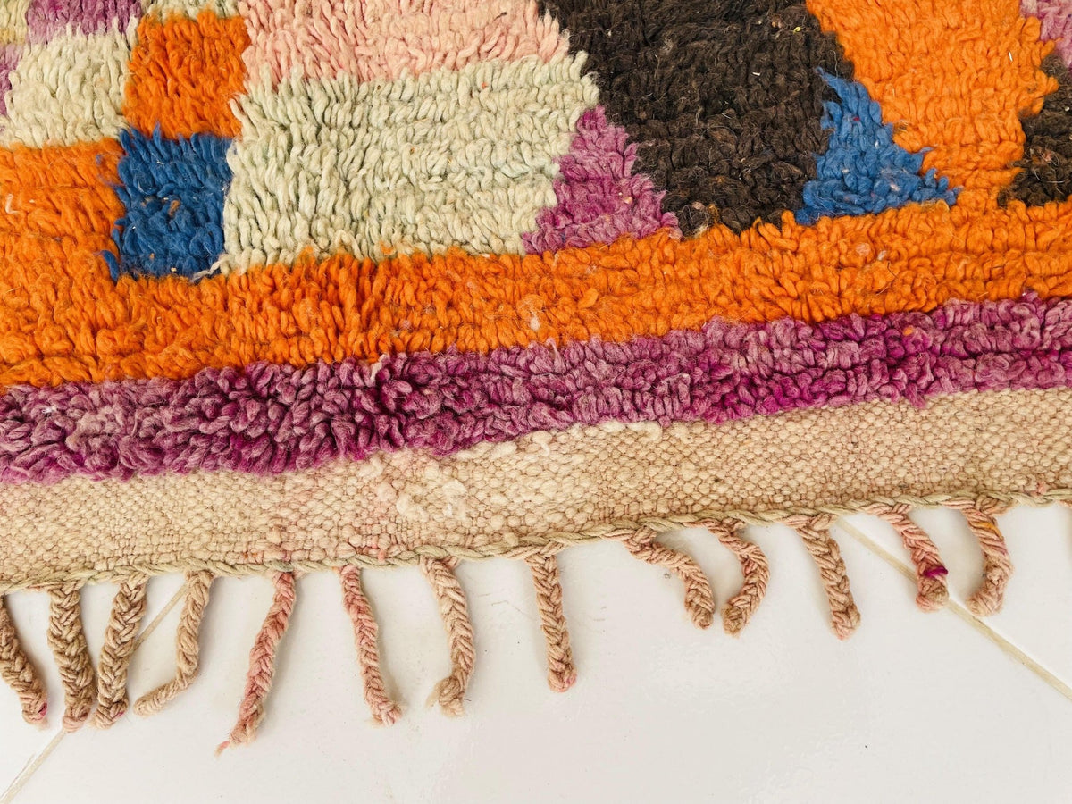 Detail close-up of the fringe edge of a vintage Moroccan rug with colorful patterns.