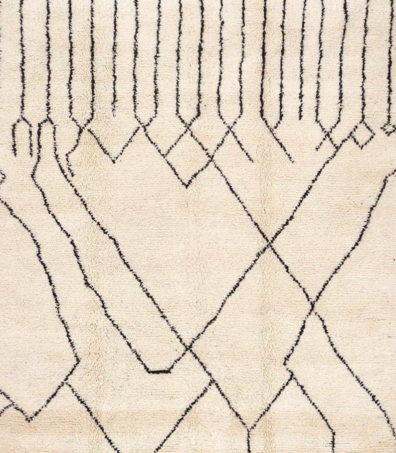 Side view of an off-white Beni Ourain rug highlighting its geometric pattern and fringe edges.