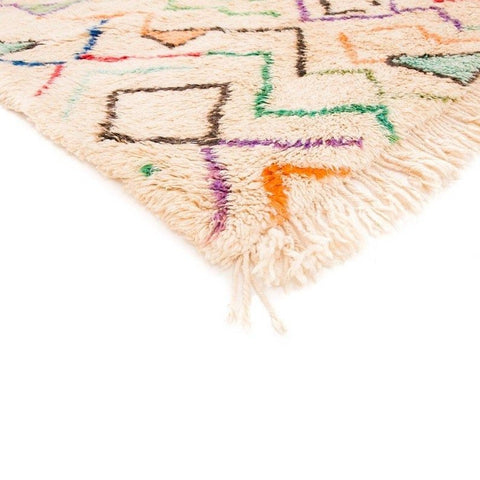 Close-up detail of a Moroccan area rug showcasing colorful patterns with fringe edges in cream, orange, blue, and green.