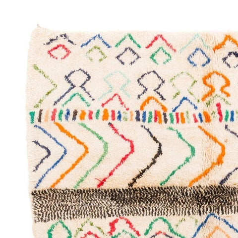 Close-up detail of a Moroccan area rug with zigzag patterns and fringe edges in cream, orange, blue, and green.