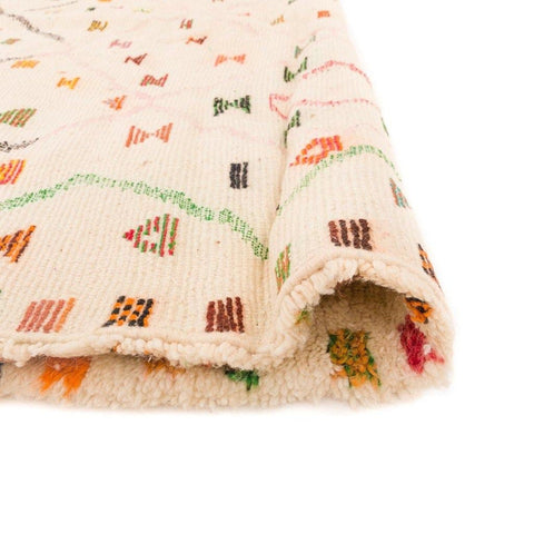 Close-up of a colorful patterned rug displaying geometric patterns in cream, orange, green, and red.