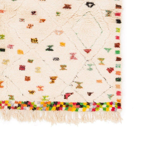 Detail view of a colorful patterned rug featuring fringe edges and colorful dots.