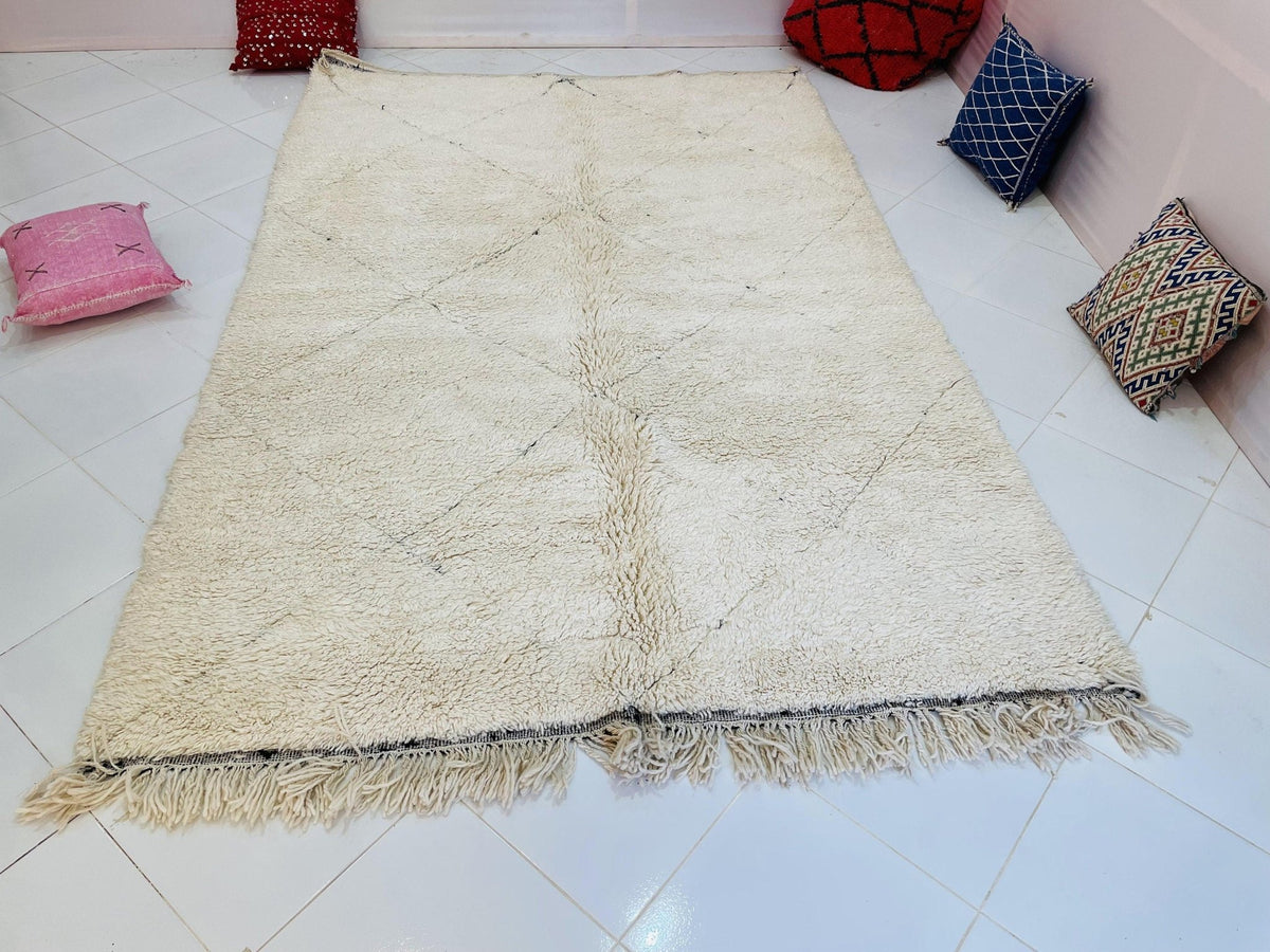 Front view of a cream and beige Moroccan rug featuring fringed edges in a studio environment.