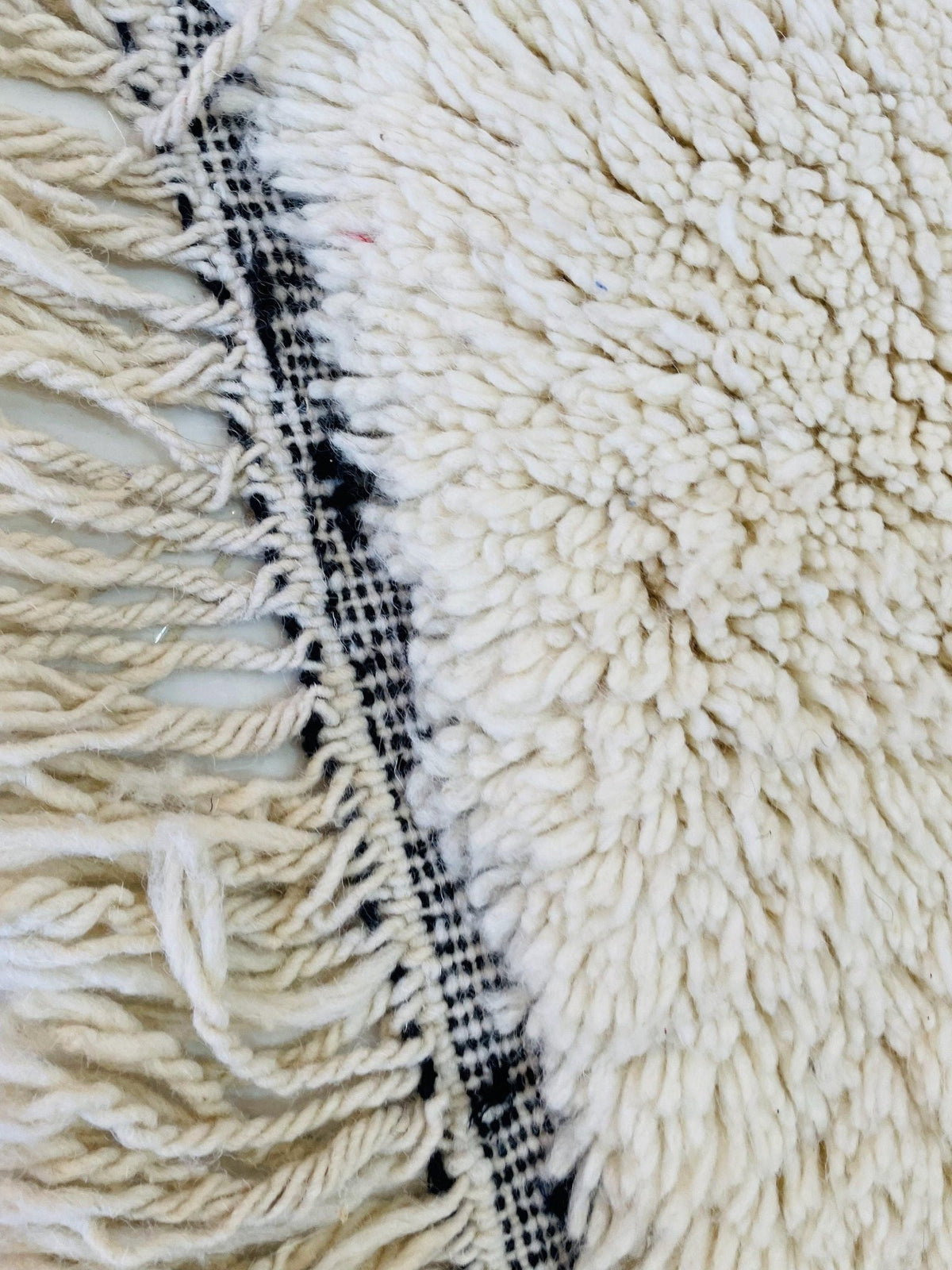 Detail shot of a white wool rug with a fringe edge and textured surface.