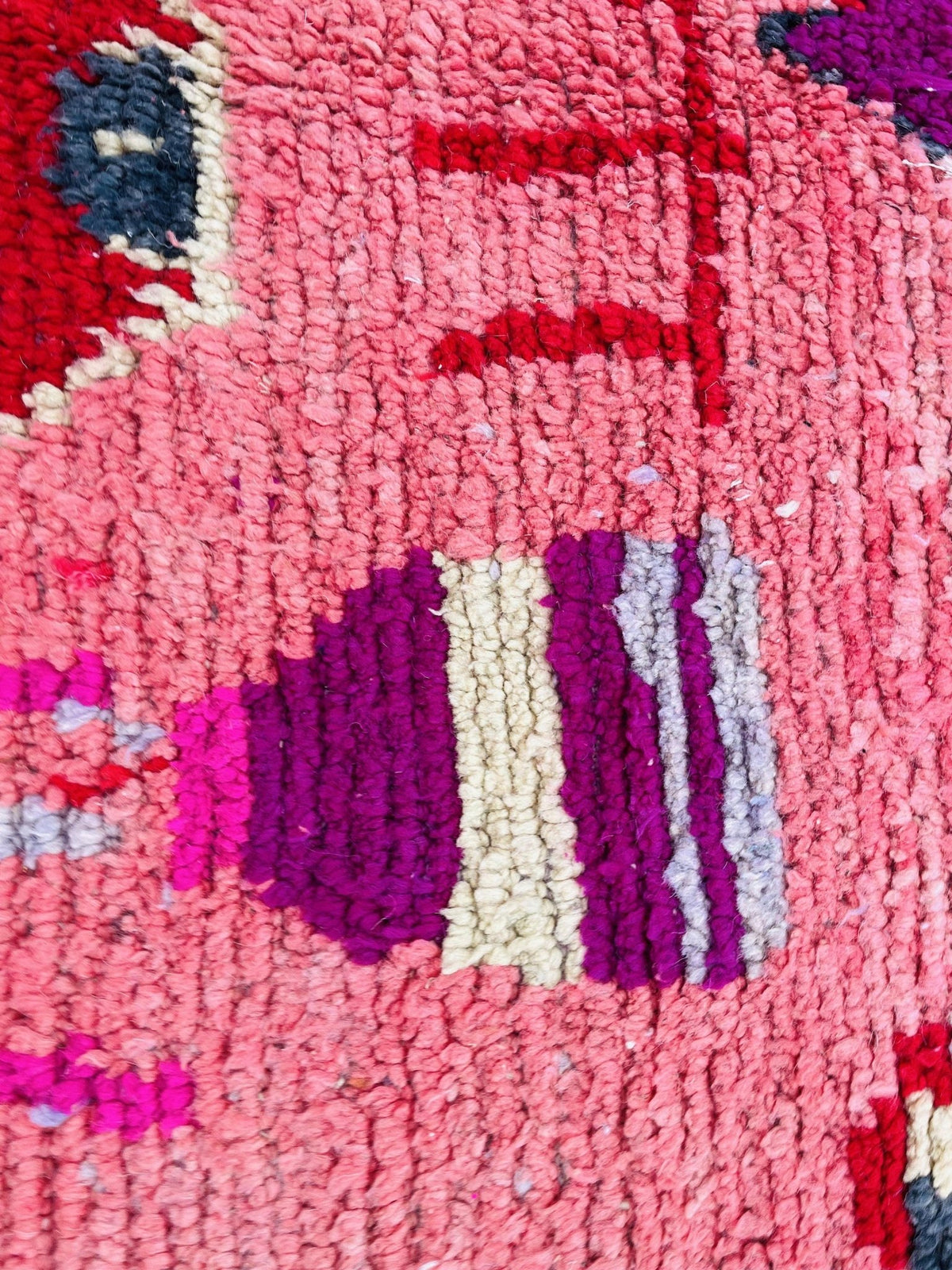 Detail close-up of a pink vintage Moroccan rug displaying abstract designs and rich colors.