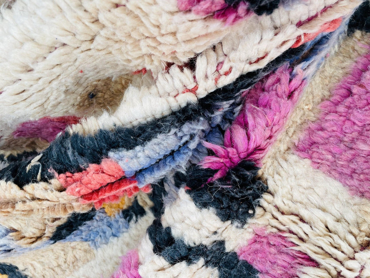 Detail shot of a vintage Moroccan rug with tribal patterns and a soft texture in pink and blue.