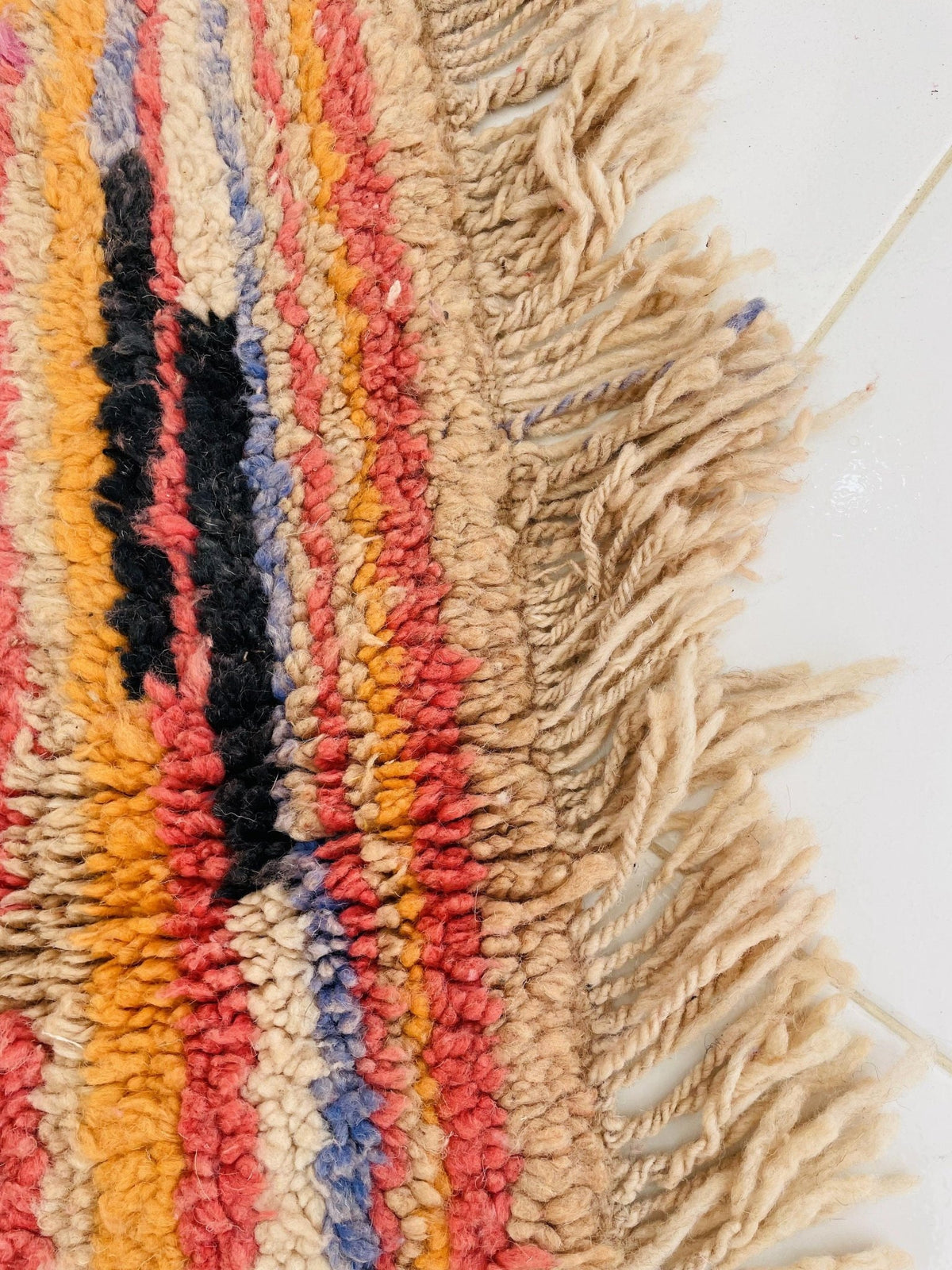 Close-up of a vintage Moroccan rug featuring colorful stripes and fringe edges in orange and red.