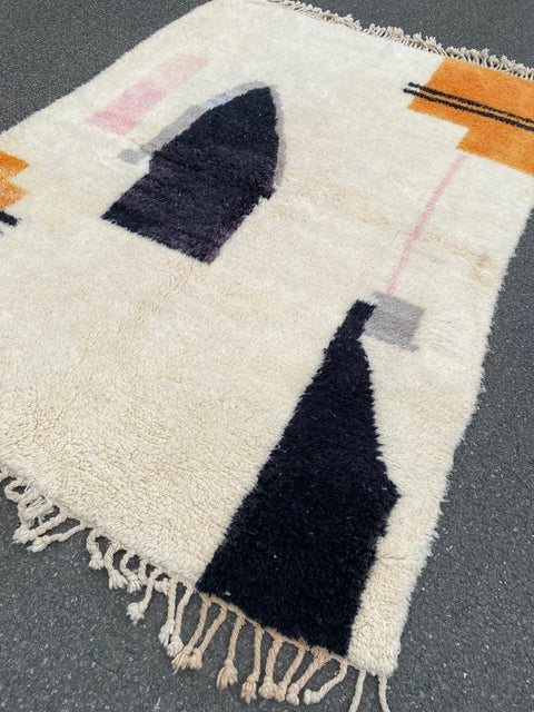 Detail close-up of the abstract design rug displaying geometric patterns and fringe edges in black, orange, and white.