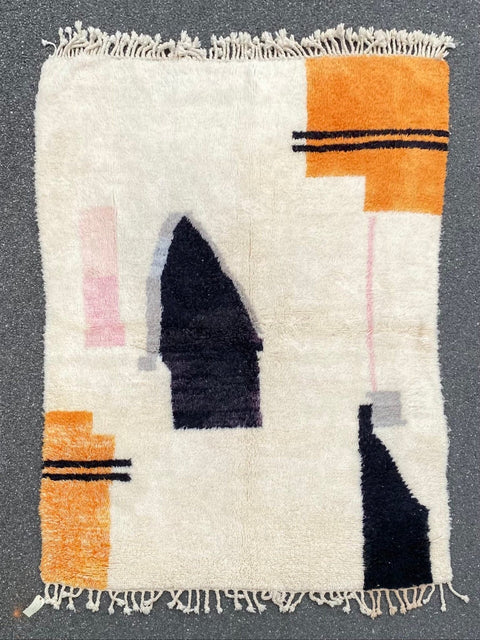 Close-up view of the abstract design rug featuring geometric patterns and fringe edges in black, orange, and pink.