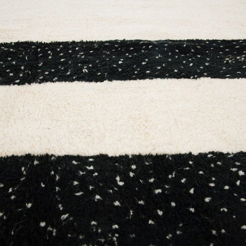 Lifestyle shot of the black and cream striped Moroccan rug laid flat on a white surface.