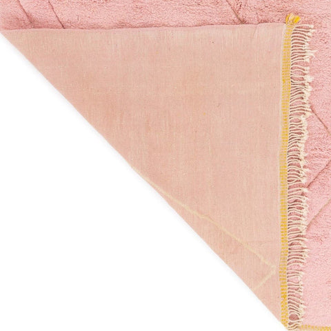 Close-up detail of the pink rug corner with geometric pattern and soft fabric.