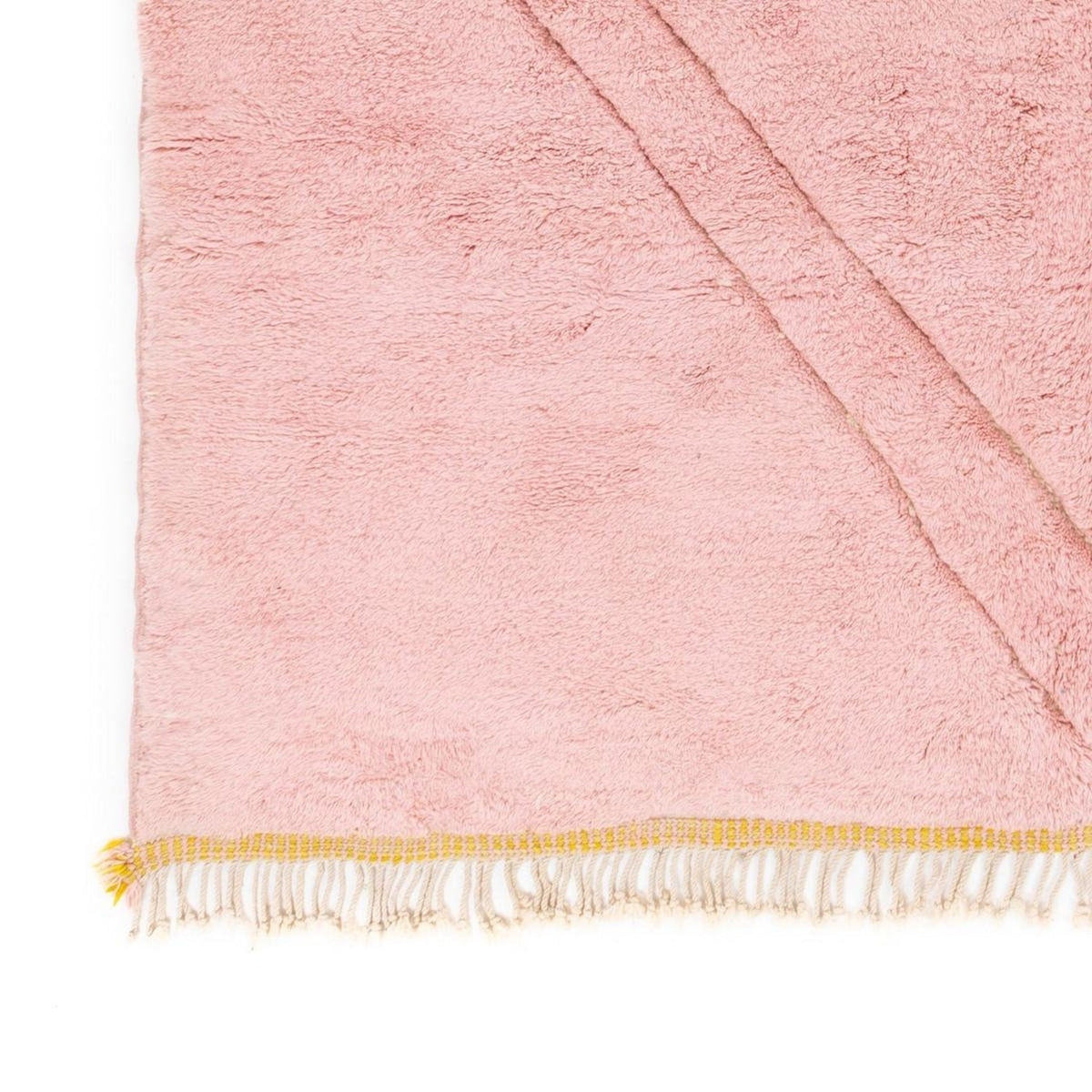 Close-up detail of the pink and yellow rug with fringe detail and soft texture.