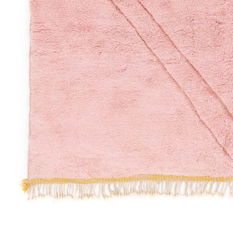 Close-up detail of the pink and yellow rug with fringe detail and soft texture.